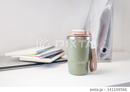 Reusable travel mug on workspace desk with notebooks minimal home office concept 141109568