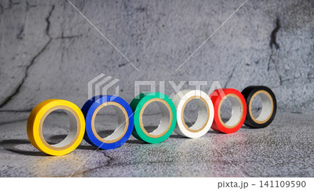 multicolored rolls of electrical tape stand vertically in a row on a gray concrete surface 141109590