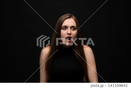 Young woman having an unexpected shocking reaction, expressing surprise and sudden fear looking away on dark background Young woman having an unexpected shocking reaction, expressing surprise and sudden fear looking away on dark background 141109642