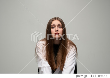 Young woman feeling sad and tired, sitting in a studio, looking at the camera with a deflated expression Young woman feeling sad and tired, sitting in a studio, looking at the camera with a deflated expression 141109647