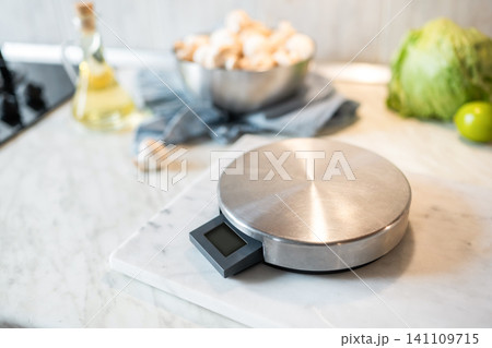 Digital kitchen scale on marble surface with cooking ingredients in background 141109715