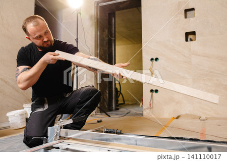 Construction worker checking ceramic tile before cutting it with tile cutter Construction worker checking ceramic tile before cutting it with tile cutter 141110017