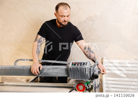 Construction worker using tile saw cutting machine preparing ceramic tiles for bathroom renovation Construction worker using tile saw cutting machine preparing ceramic tiles for bathroom renovation 141110026