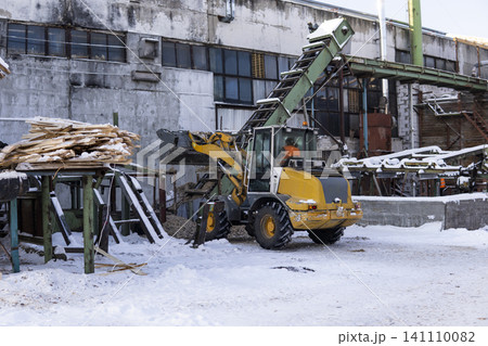 Front loader picking up wood chips in a sawmill sorting area on a snowy winter day, recycling wood waste 141110082