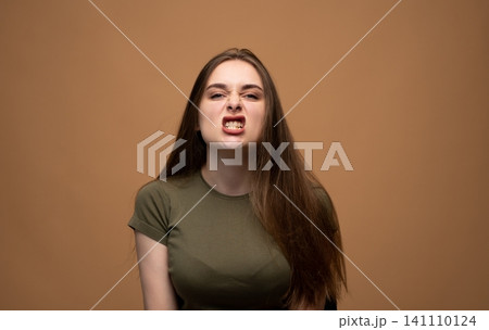 Young woman grimacing, expressing anger, frustration, and disgust, clenching teeth in a confrontational emotion Young woman grimacing, expressing anger, frustration, and disgust, clenching teeth in a confrontational emotion 141110124