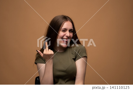Young woman winking and playfully sticking out her tongue, showing a rude middle finger gesture to the viewer Young woman winking and playfully sticking out her tongue, showing a rude middle finger gesture to the viewer 141110125