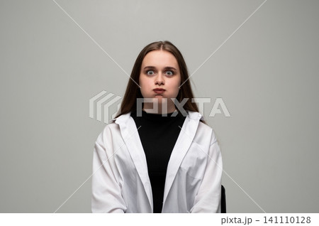 Young woman puffing cheeks and widening eyes, creating a funny face, showing humorous and playful expression Young woman puffing cheeks and widening eyes, creating a funny face, showing humorous and playful expression 141110128