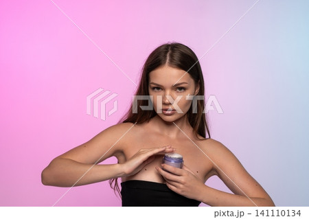 Young woman applying face cream to face, demonstrating skincare routine and beauty treatment for hydrated skin 141110134