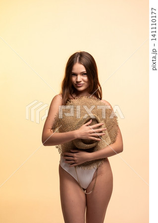 Young woman posing in swimwear with a large straw hat, representing summer fashion, confidence, and trendy beach style Young woman posing in swimwear with a large straw hat, representing summer fashion, confidence, and trendy beach style 141110177