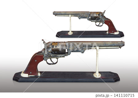 side view two antique and old brass guns with a brown leather grip, placed on a wooden stand against a white background 141110715