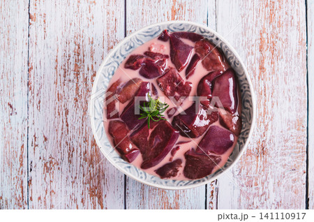Close up of raw pork liver soaked in milk in a bowl on the table top view Close up of raw pork liver soaked in milk in a bowl on the table top view 141110917
