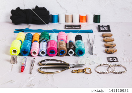 A set of spools of multi-colored threads and sewing supplies on a table A set of spools of multi-colored threads and sewing supplies on a table 141110921