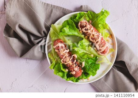 Close up of grilled sausage with sauce and croutons on lettuce leaves on a plate on the table top view Close up of grilled sausage with sauce and croutons on lettuce leaves on a plate on the table top view 141110954