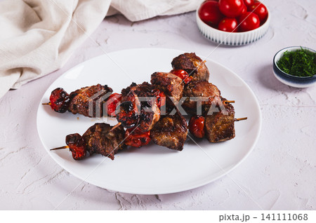 Grilled meat baked in spices with cherry tomatoes on skewers on a plate on the table 141111068