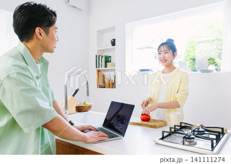 キッチンでメールチェックをする男性と朝食を作る女性 キッチンでメールチェックをする男性と朝食を作る女性 141111274