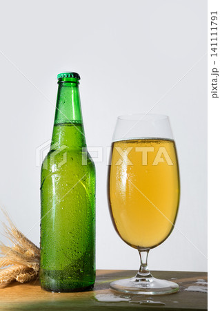 Cold beer bottle with condensation and glass on table 141111791