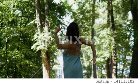 A woman stands with arms raised in a serene forest during a peaceful summer day, surrounded by lush greenery and a clear blue sky. The rear view showcases the fabric ofa. A woman stands with arms raised in a serene forest during a peaceful summer day, surrounded by lush greenery and a clear blue sky. The rear view showcases the fabric ofa. 141113102