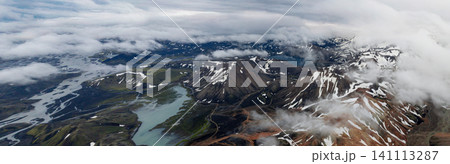 Spectacular aerial panorama of colorful rhyolite mountains, glacial rivers, alpine lakes and drifting clouds in Landmannalaugar, showcasing Iceland Highlands from above. Spectacular aerial panorama of colorful rhyolite mountains, glacial rivers, alpine lakes and drifting clouds in Landmannalaugar, showcasing Iceland Highlands from above. 141113287