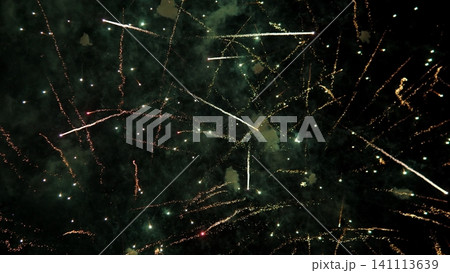 Bright fireworks burst across dark night sky, scattering long glowing streaks, sparkling trails, and smoky clouds in festive celebration scene with dramatic contrast and vivid 141113639