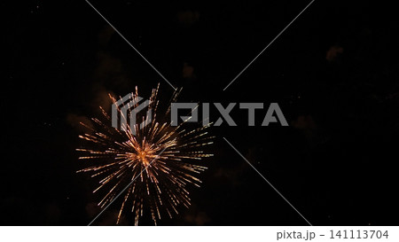 Golden fireworks explode in dark night sky, sending bright radiant trails outward from glowing center with faint smoke clouds and scattered sparks creating dramatic festive scene Golden fireworks explode in dark night sky, sending bright radiant trails outward from glowing center with faint smoke clouds and scattered sparks creating dramatic festive scene 141113704