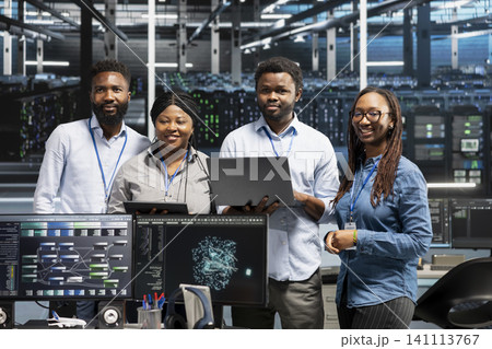 Smiling server room specialists working with machine learning models to review extensive data sets. 141113767