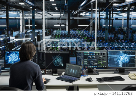 IT specialist working with computer in high tech computing hub with equipment supporting deep learning scientific simulations with computer scientist in server facility doing checkup on rackmounts. IT specialist working with computer in high tech computing hub with equipment supporting deep learning scientific simulations with computer scientist in server facility doing checkup on rackmounts. 141113768