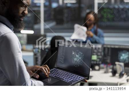 Server room admin working with AI visual analytics tools on laptop to detect hardware faults. Server room admin working with AI visual analytics tools on laptop to detect hardware faults. 141113954