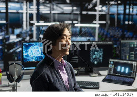 System administrator in server room working with computer, managing AI training data sets. 141114017