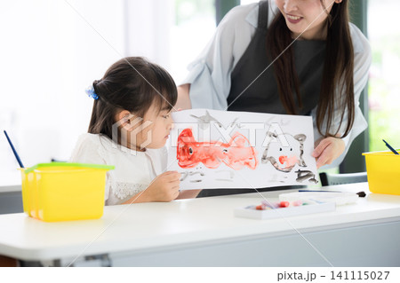 よくできました~と褒められる、母親や先生に見守られながら美術や図工で水彩画を描く小学生位の女の子 よくできました~と褒められる、母親や先生に見守られながら美術や図工で水彩画を描く小学生位の女の子 141115027