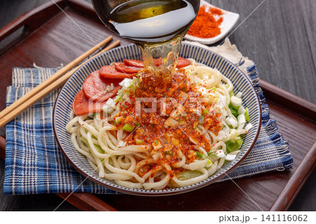 lifting Shaanxi hand-pulled noodles with chopsticks from a bowl, featuring spicy chili and sausage topping, close-up shot lifting Shaanxi hand-pulled noodles with chopsticks from a bowl, featuring spicy chili and sausage topping, close-up shot 141116062