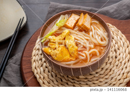 a warm bowl of Chinese hand-pulled noodle soup with fried egg and tofu puffs on a woven placemat a warm bowl of Chinese hand-pulled noodle soup with fried egg and tofu puffs on a woven placemat 141116068