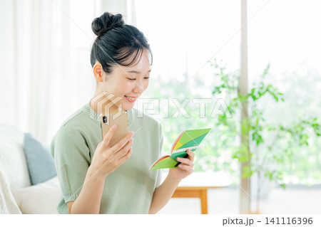 スマホと通帳を見る若い女性 141116396