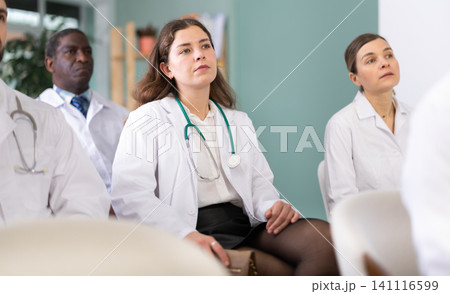 Female doctor listens to lecture with colleagues in auditorium Female doctor listens to lecture with colleagues in auditorium 141116599