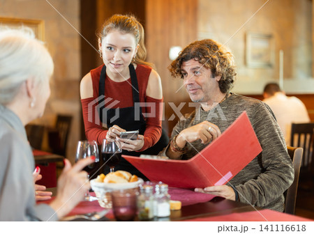 Young waitress taking order from adult couple in restaurant Young waitress taking order from adult couple in restaurant 141116618