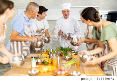 Adult male cook teaches cooking to group of people 141116673