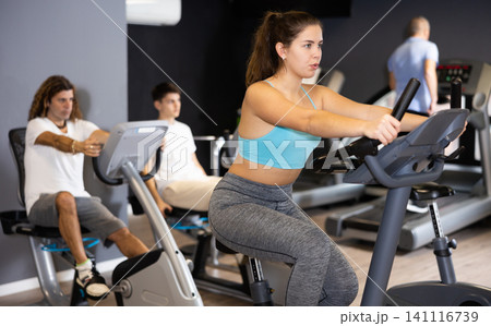 Young girl working out on stationary bicycle in gym Young girl working out on stationary bicycle in gym 141116739