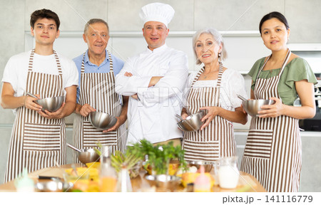 Successful male chef posing with group at cooking course Successful male chef posing with group at cooking course 141116779