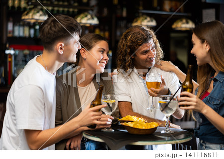 Cheerful adult friends talking and drinking beer at table in pub Cheerful adult friends talking and drinking beer at table in pub 141116811