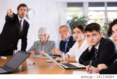 Frustrated guy sitting in office with coworkers and irritated boss Frustrated guy sitting in office with coworkers and irritated boss 141116884