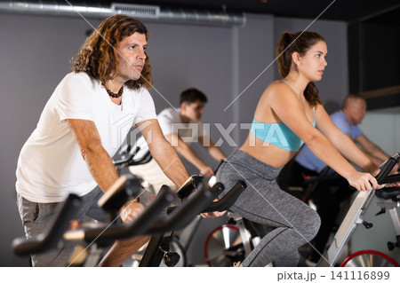 Man and woman taking indoor cycling class at fitness center, doing cardio riding bike 141116899