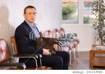 Middle-aged male visitor sitting on the bench in waiting room of clinic Middle-aged male visitor sitting on the bench in waiting room of clinic 141117050