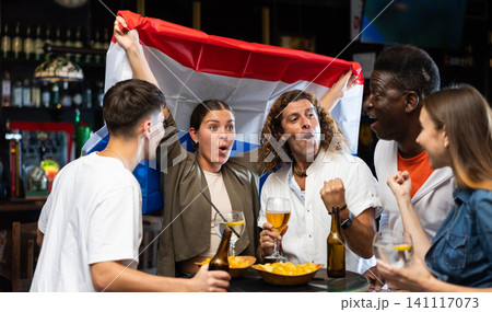 Young adults watching football championship in sports bar, supporting team from Netherlands Young adults watching football championship in sports bar, supporting team from Netherlands 141117073