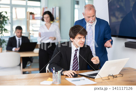 Elderly man helping young male colleague work on laptop 141117126