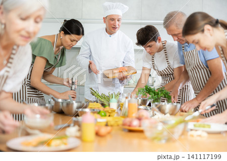 Experienced male chef teaching to cook salmon at group culinary class 141117199