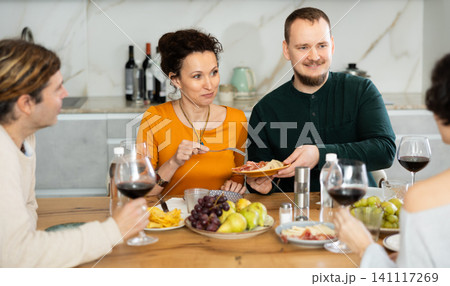 Two married couples are sitting at table, enjoying food and wine, chatting, talking, laughing. 141117269
