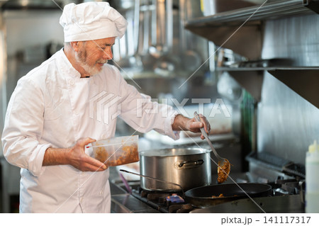 Mature man cook in kitchen is working near stove Mature man cook in kitchen is working near stove 141117317
