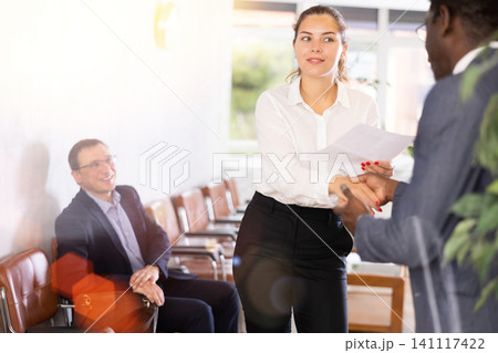 Young woman handshaking with other person in waiting room 141117422