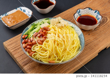 northeast Chinese style cold yellow noodles with peanuts, cucumber, and dipping sauces on a wooden board 141118234