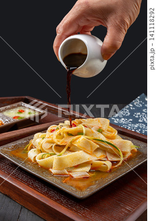 close-up of a hand pouring black vinegar sauce onto Chinese Liangpi cold noodles 141118292