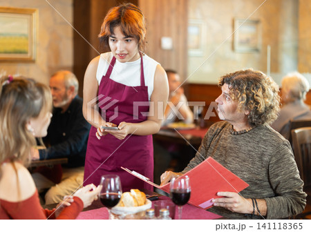At cafe, Filipino girl waitress communicates with man and mature woman customer, accepts order At cafe, Filipino girl waitress communicates with man and mature woman customer, accepts order 141118365